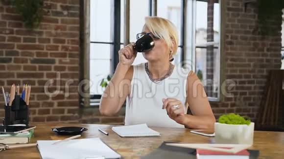 漂亮的女人正在检查日记中的报告而喝咖啡坐在办公桌后面的家庭办公室印度支视频的预览图