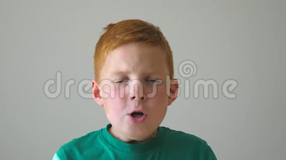 一个可爱的红发男孩抓住他的头在他的脸上表现出喜悦年轻的孩子带着摄像机视频的预览图