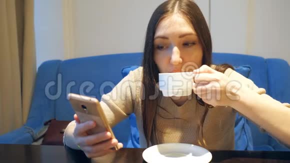 快乐的年轻女子坐在咖啡店里用智能手机发短信视频的预览图