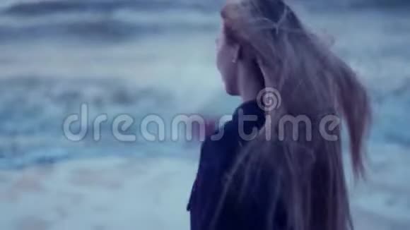 美丽的女孩看着大海转向相机她的头发在背景下发展风波浪视频的预览图