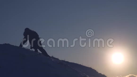 冬季夕阳下雄性登山者登上雪山顶的剪影在雪地里旅行视频的预览图