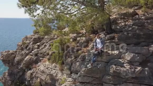 海边岩石峭壁上年轻旅行者的鸟瞰图视频的预览图
