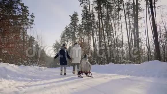 带着孩子的女人走在穿过森林的雪道上视频的预览图