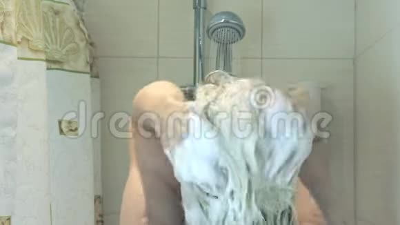 在浴室里金发女人在头发上泡发水从淋浴头上掉下来的水洗头和身体护理视频的预览图