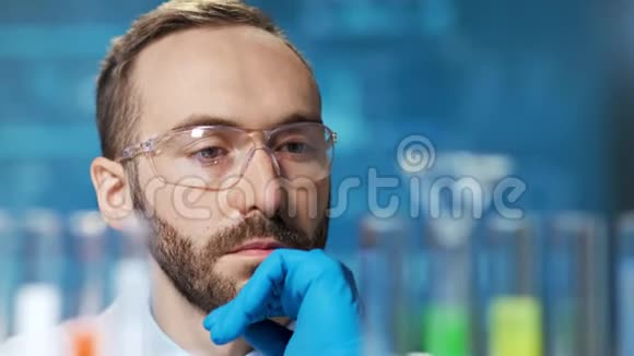 仔细思考的男性化学工作者用五颜六色的液体样品看着烧杯的特写视频的预览图