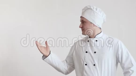 一个穿着厨师衣服和帽子的聪明厨师站在一个明亮的房间里把他的手放在一边视频的预览图