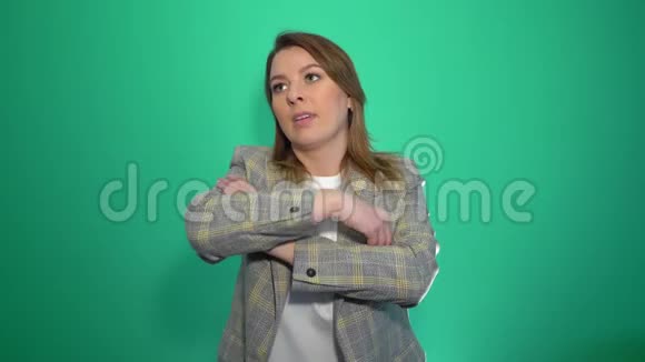 穿着双臂交叉摆姿势在绿色背景下看着摄像机的一个穿着紧身衣的女人视频的预览图