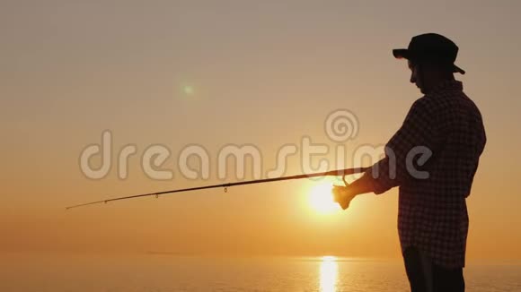 日落时在海滩上钓鱼的年轻渔夫的剪影侧视图视频的预览图
