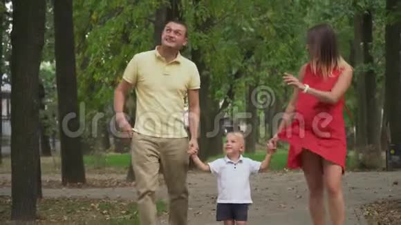 父母牵着男孩手在公园里散步视频的预览图