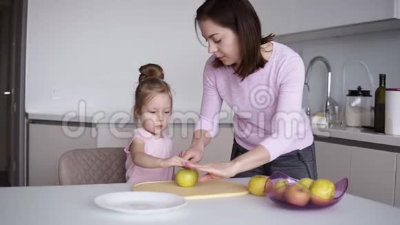 妈妈和女儿在家做健康的食物玩得开心年轻女子在面前的桌子上切黄苹果视频的预览图