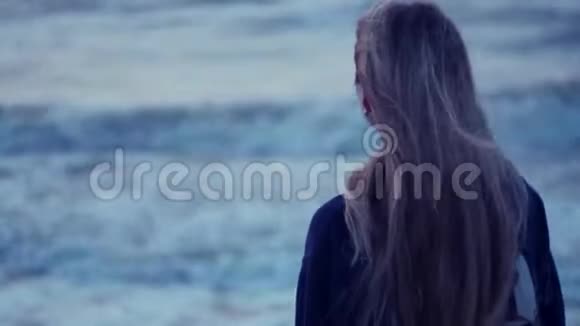 美丽的女孩看着大海转向相机她的头发在背景下发展风波浪视频的预览图