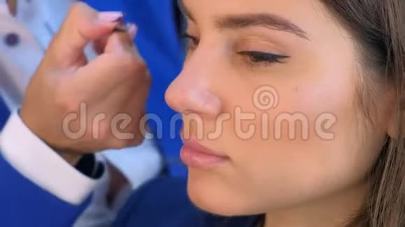 化妆师将人造睫毛涂在女孩模特眼睛和面部特写上视频的预览图