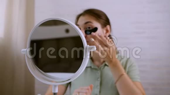 女孩用黑色补丁在她的眼睛下微笑坐在镜子对面健康的生活方式青春面部视频的预览图