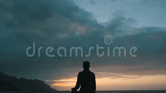一位妇女坐在岩石上的剪影日落时在加那利群岛特内里费的贝尼霍海滩观察海浪视频的预览图