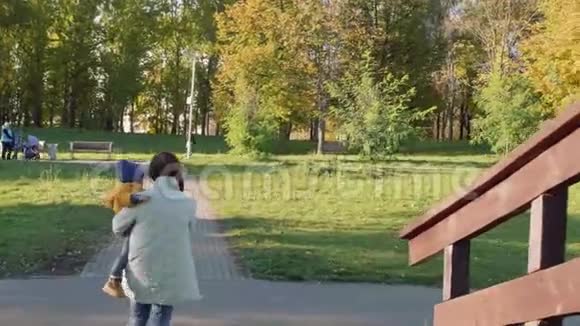 阳光明媚的一天镜头跟随着妈妈和小儿子在秋天的公园里牵手背面视频的预览图