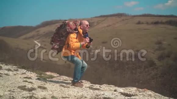 一个穿着黄色夹克和眼镜的人站在山上欣赏风景在dslr相机上拍照视频的预览图