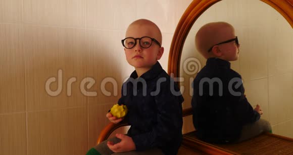 小金发男孩坐在梳妆台上拿着镜子吃了一个苹果孩子在家玩得很开心视频的预览图