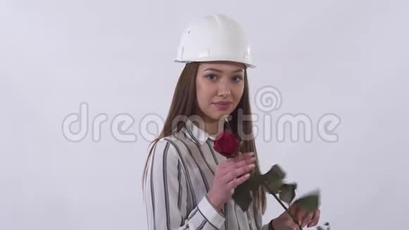戴着头盔的年轻漂亮女人手里拿着一朵红色的玫瑰在工作室里被孤立在白色背景上非常高兴视频的预览图