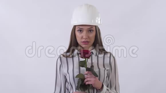 一位戴着白色头盔手里拿着一朵红玫瑰的可爱年轻女子在白色背景下被孤立她非常高兴视频的预览图
