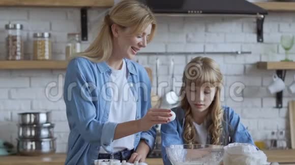 妈妈和女儿正在厨房准备一个馅饼妈妈在大碗里敲一个鸡蛋慢速射击大型视频的预览图
