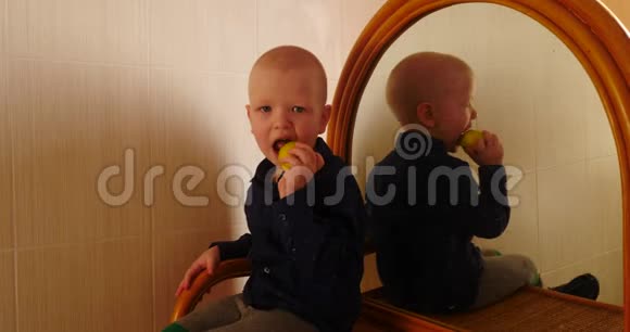 小金发男孩坐在梳妆台上拿着镜子吃了一个苹果孩子在家玩得很开心视频的预览图