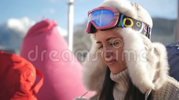 一个穿着毛衣和帽子的迷人女孩坐在滑雪场的户外咖啡馆里在一张自拍上视频的预览图