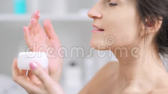 贴身放松的年轻女性在颈部涂抹白色抗龄保湿霜视频的预览图