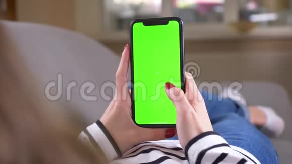 特写后景拍摄女性在手机上滑动绿色屏幕将其垂直放置在沙发上视频的预览图