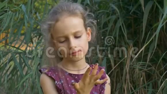 美丽的金发女郎穿着紫罗兰色的连衣裙扎着马尾辫正在公园里吃一块巧克力糖果一天后糖视频的预览图