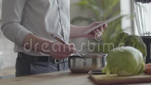不可辨认的男人在衬衫上煮汤检查食谱在厨房里的平板电脑上健康观念视频的预览图