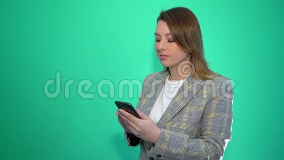 失望的悲伤金发女孩在手机上发短信而站在绿色的背景上孤立视频的预览图