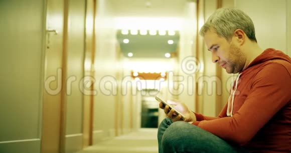 穿休闲服装的帅哥在酒店走廊里用智能手机视频的预览图