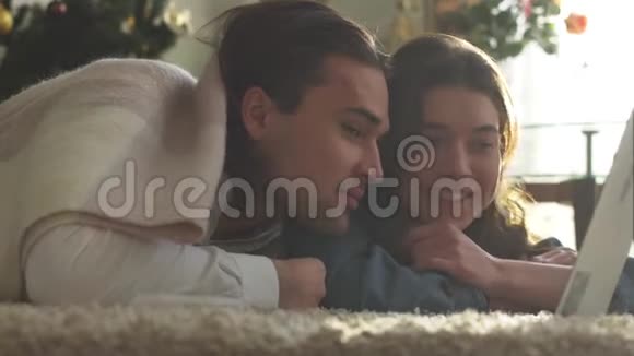 年轻人和女孩被一条毯子覆盖在地板上看着家里的笔记本电脑亲密的情侣相爱视频的预览图