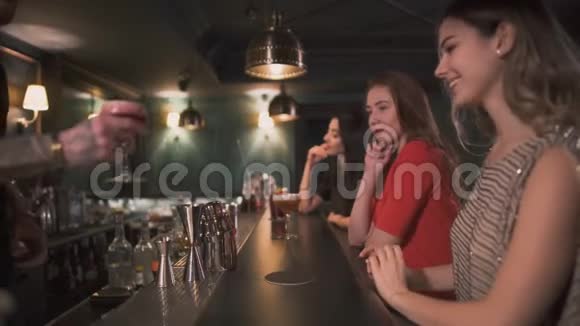 三个年轻漂亮的女朋友穿着晚礼服坐在酒吧柜台边戴着眼镜喝着鸡尾酒视频的预览图
