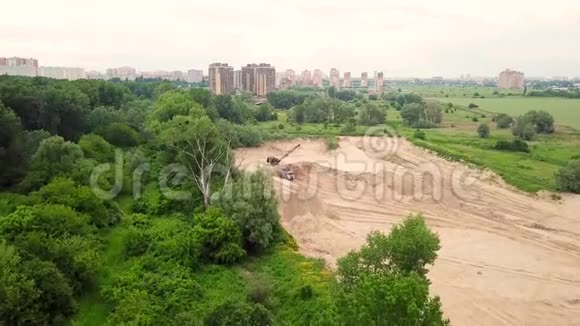 从上往下看挖掘机将沙子倒入卡车靠近树木和城市建筑视频的预览图