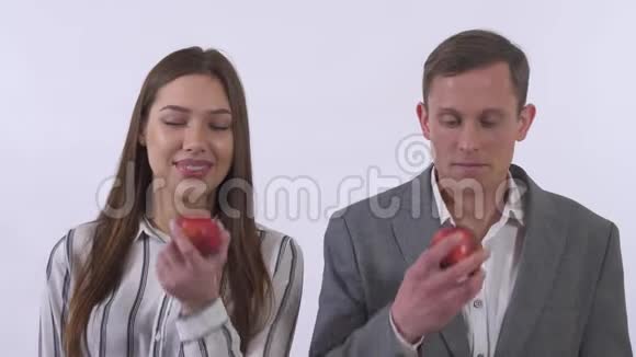微笑的年轻夫妇男人和女人吃红苹果白色背景上孤立的男人和女人的肖像视频的预览图