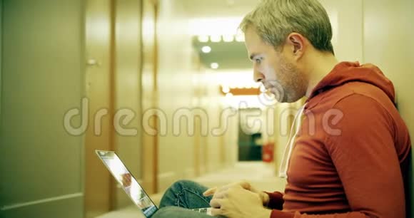灰发男子穿着便装在酒店走廊的笔记本电脑上工作视频的预览图