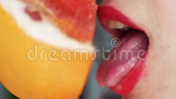 女人舌头舔葡萄柚一个女孩的肖像明亮的红色嘴唇舔一个粉红色的葡萄柚关门视频的预览图