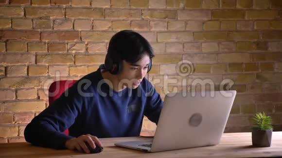 年轻迷人的韩国商人戴着笔记本电脑的耳机兴奋地笑了起来视频的预览图
