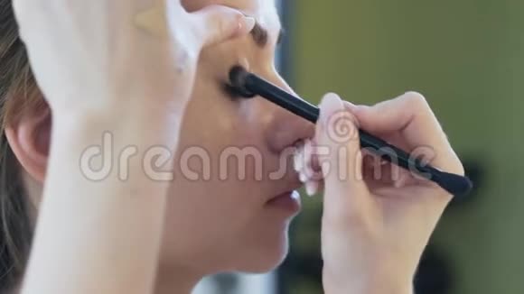 特写裁剪框动作缓慢化妆师用铅笔画女孩并用画笔在颜料上涂上阴影视频的预览图