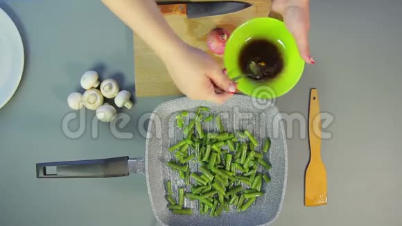 一个女人用勺子搅拌酱油把绿豆倒在锅里视频的预览图