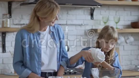 妈妈和女儿正在厨房准备一个馅饼一个女孩把面粉倒进一个大碗里慢动作射击大型视频的预览图