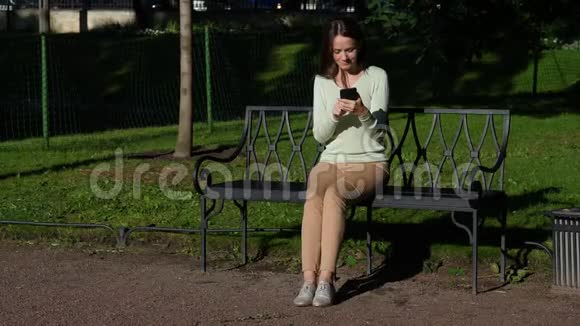 布吕内蒂女士坐在公园的长凳上用智能手机交流视频的预览图