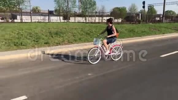 女孩骑自行车在沥青路上在她的背包后面在一个货篮里放着一束花视频的预览图