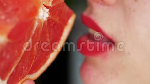 女人舌头舔葡萄柚一个女孩的肖像明亮的红色嘴唇舔一个粉红色的葡萄柚关门视频的预览图