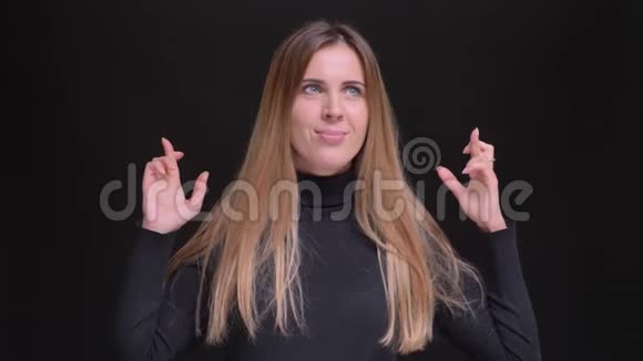 白种人长发金发金发女孩的肖像愉快地手势交叉手指标志以显示希望的黑色背景视频的预览图