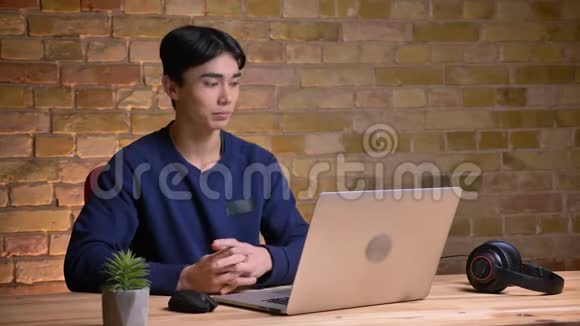 年轻迷人的韩国男学生戴上耳机在笔记本电脑上打视频电话的特写照片视频的预览图