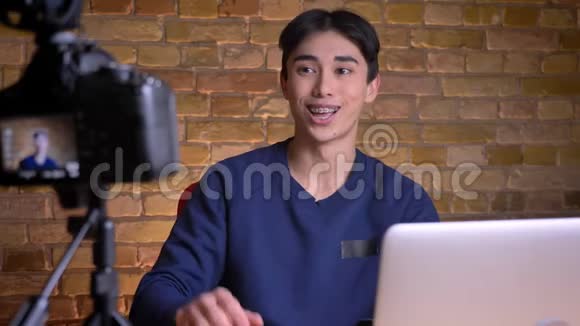 年轻的韩国男视频登记员在镜头前用手在室内打招呼的特写镜头视频的预览图