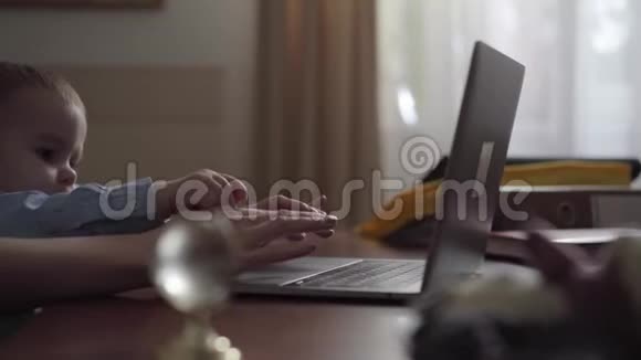 女人用手在笔记本电脑上打字孩子阻止母亲工作忙碌的年轻母亲在家工作小儿子视频的预览图