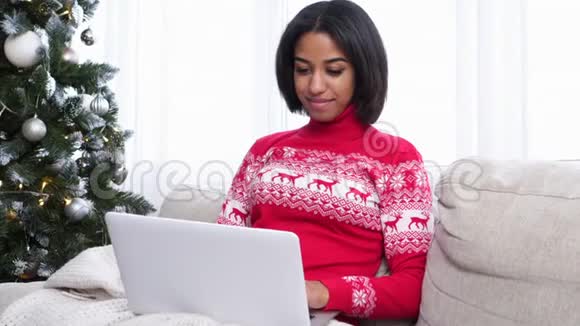 家里圣诞树旁边沙发上用笔记本电脑的少女视频的预览图